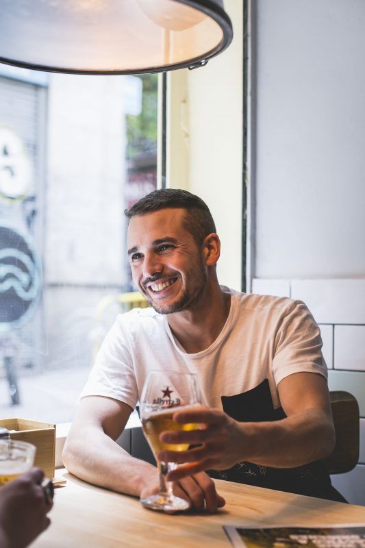 retrato de un hombre que está junto a una ventana tomando una cerveza